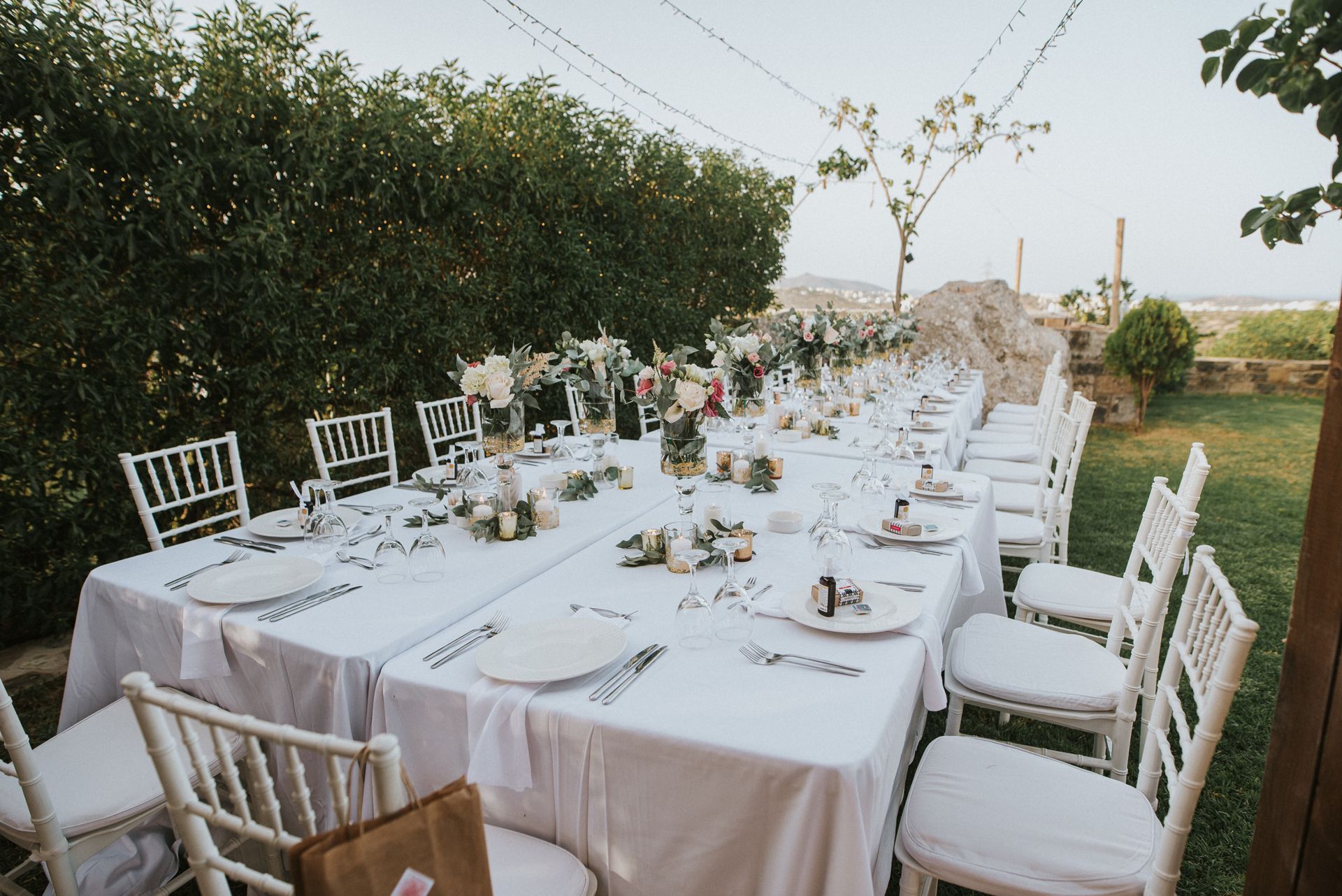 A long table with white chairs and plates set for a wedding reception