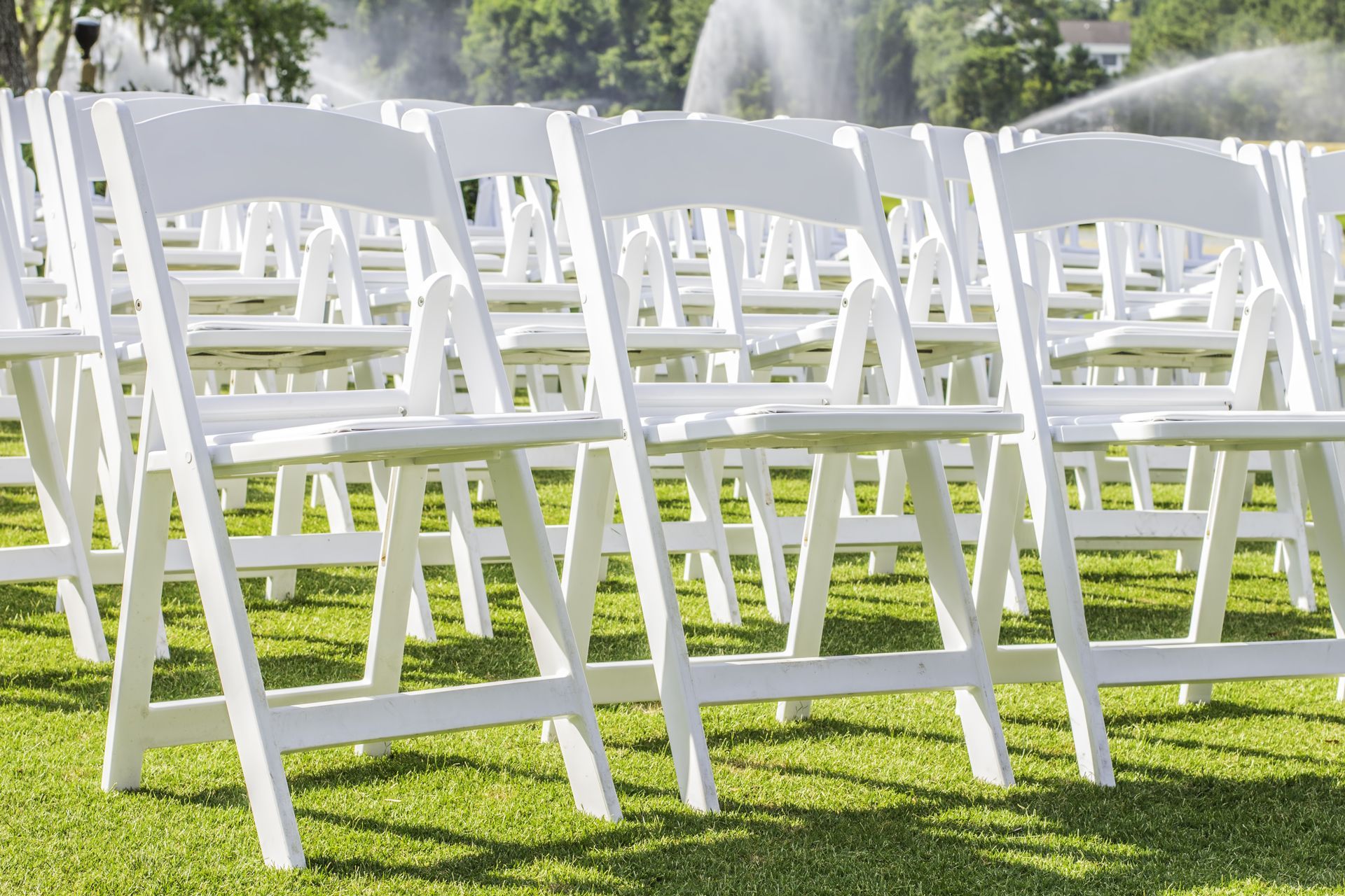 A row of white folding chairs sitting on top of a lush green field