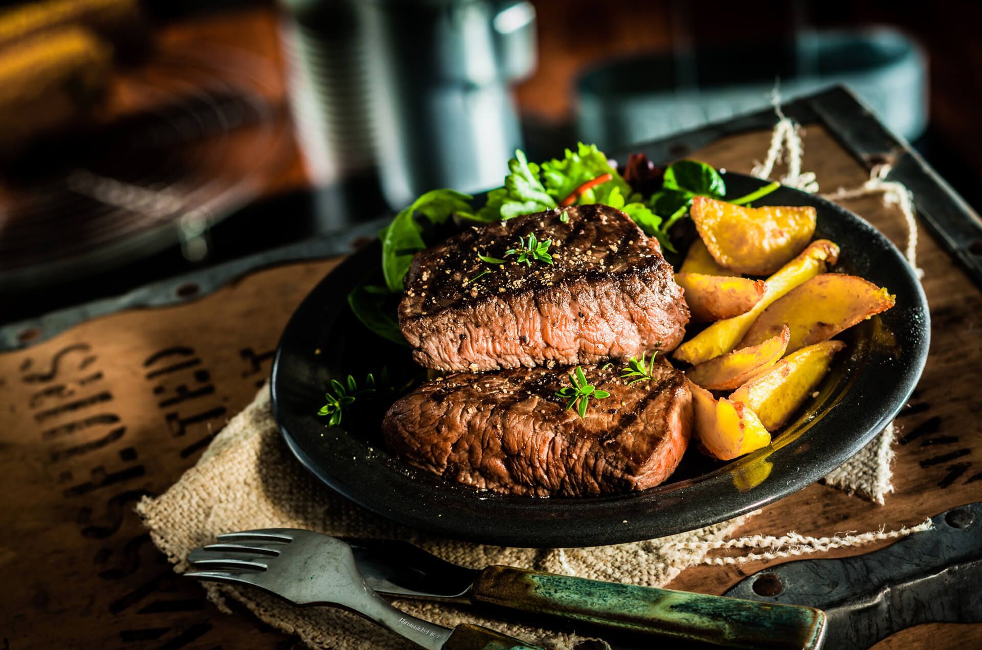 A plate of steak and potatoes on a table with a fork