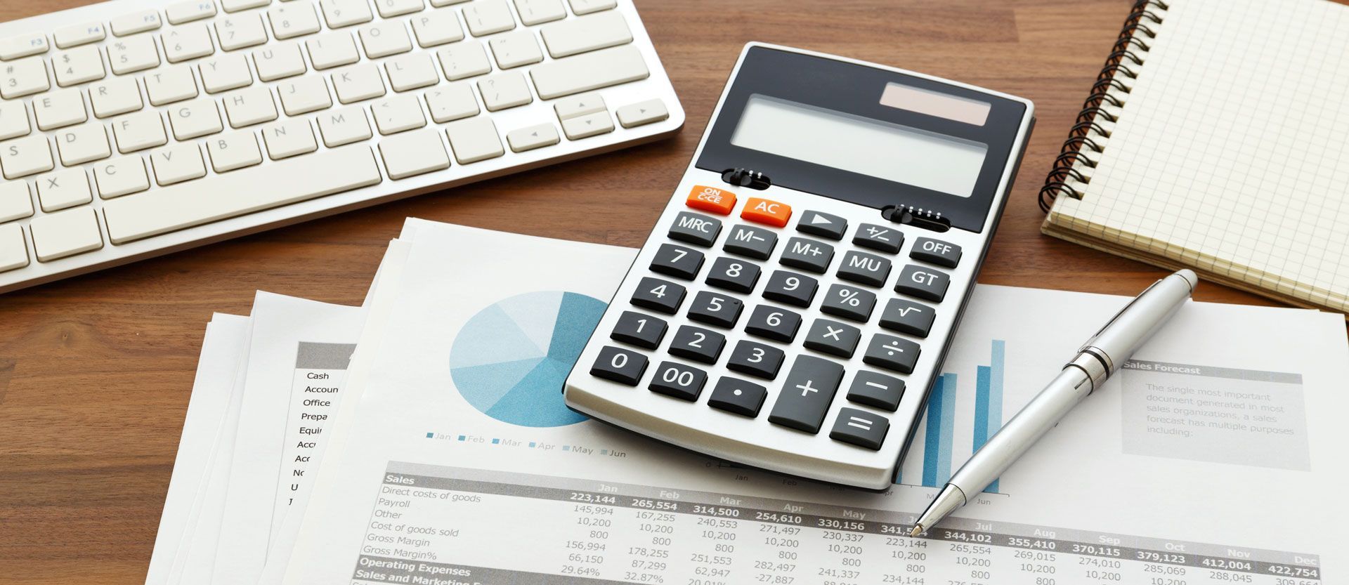 Calculator, pen, notebook, and keyboard on a desk with financial reports.