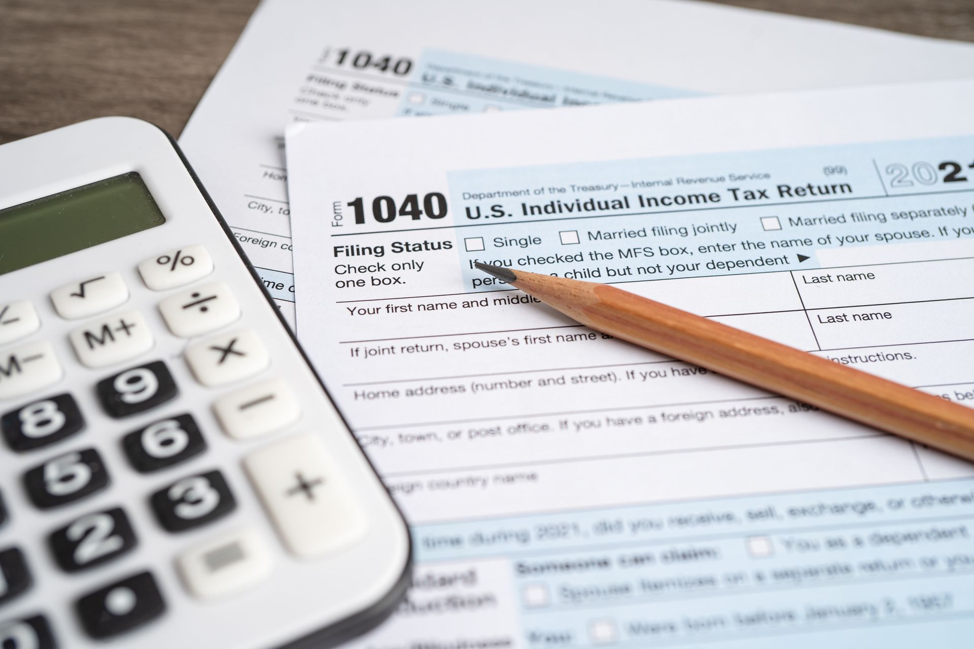 A pencil rests on a 2021 U.S. Individual Income Tax Return (Form 1040) next to a white calculator on a wooden surface.