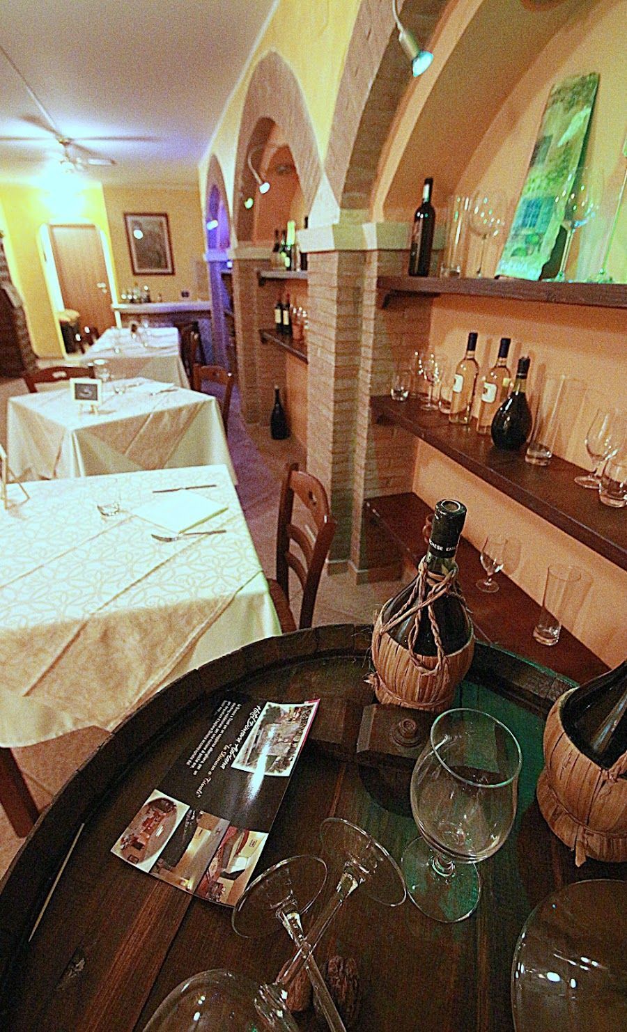 Interno di un ristorante con tavoli apparecchiati, bottiglie di vino esposte e porte ad arco.