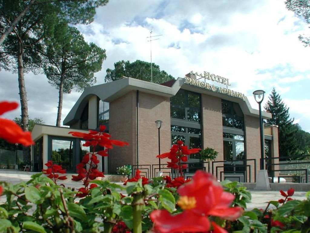 Edificio con grandi finestre e insegna, con fiori rossi in primo piano e alberi sullo sfondo.