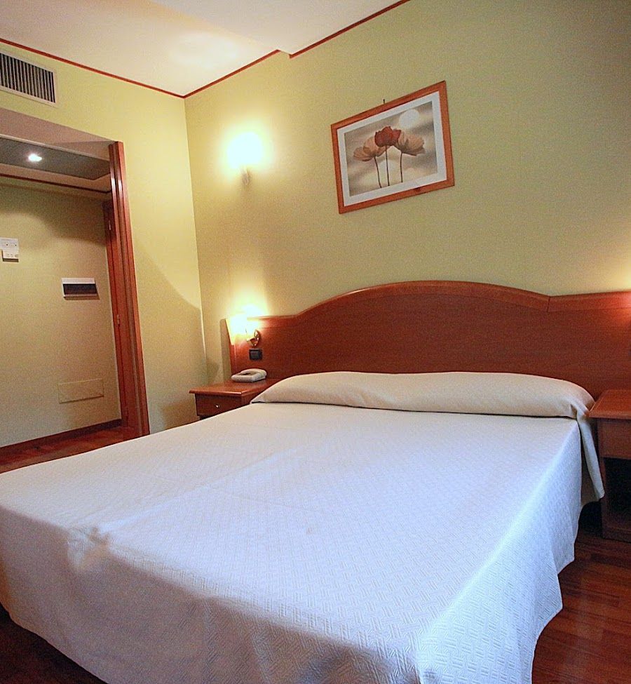 Camera d'albergo con letto, comodini e porta per il bagno. Tonalità beige e legno.