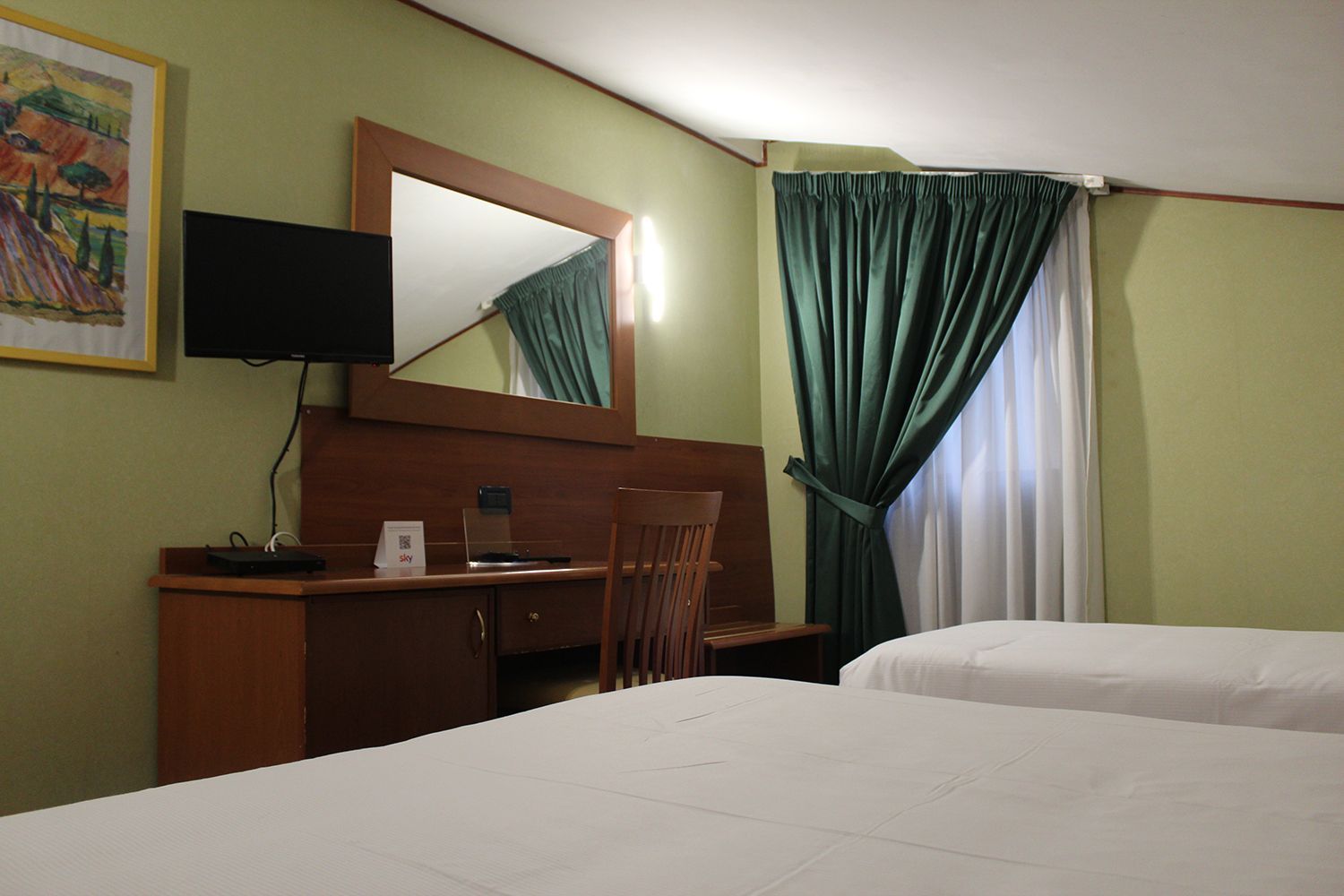 Camera d'albergo con due letti, scrivania, specchio, TV, pareti verdi e tende.