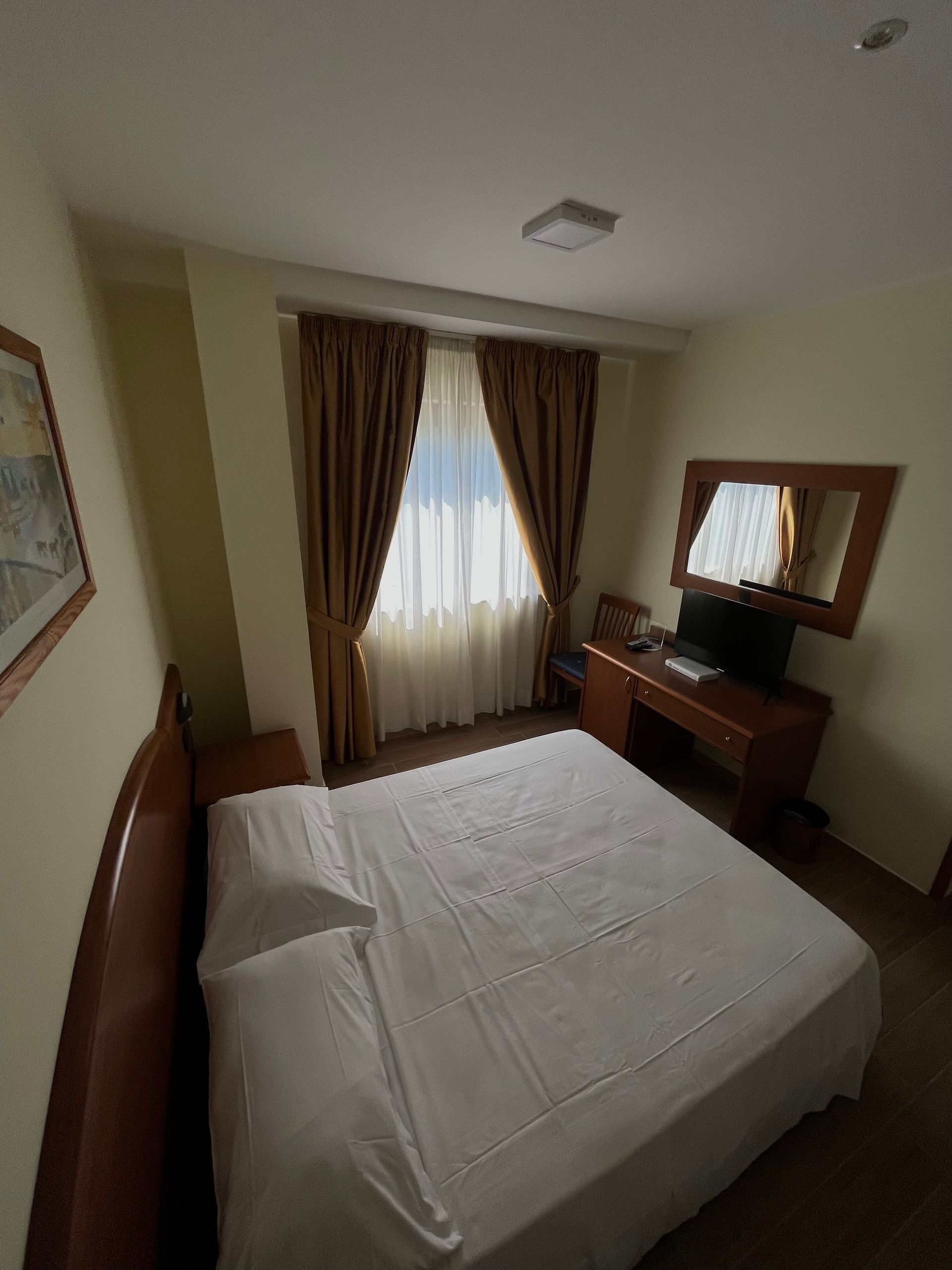 Camera da letto con letto matrimoniale, scrivania, finestra con tende e opere d'arte.