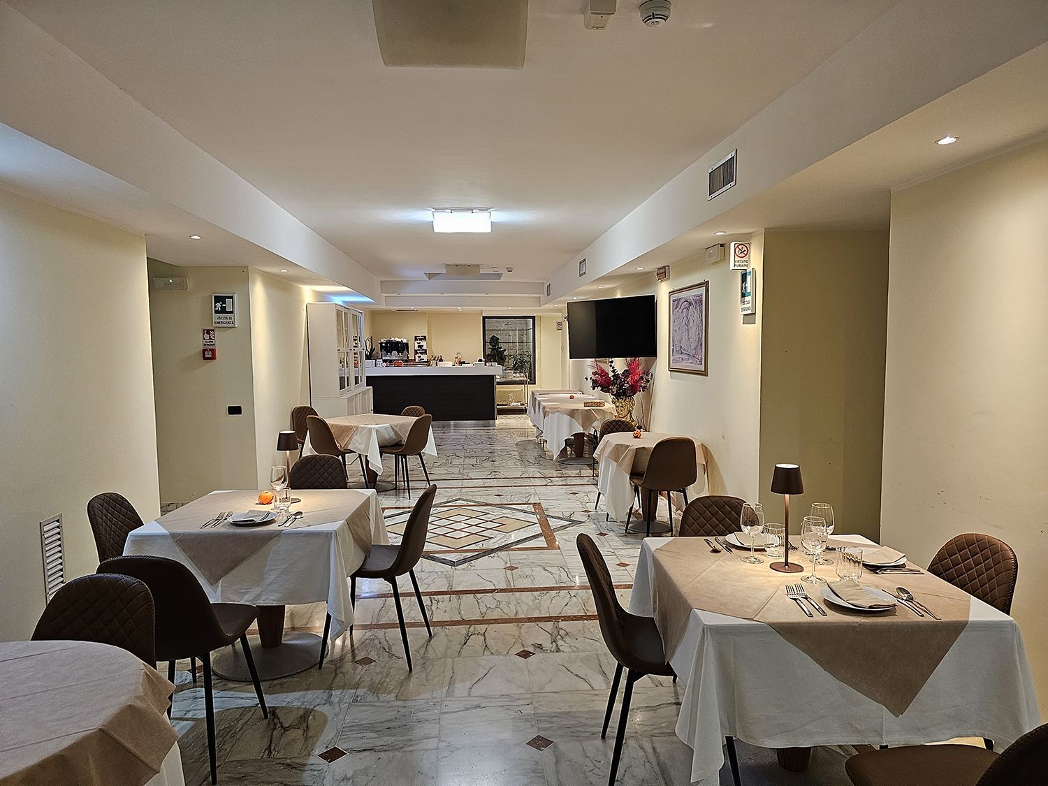 Interno di un ristorante con tavoli apparecchiati e un bar sullo sfondo.