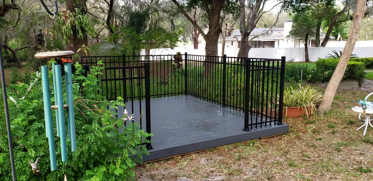 A black fence surrounds a small deck in a backyard.