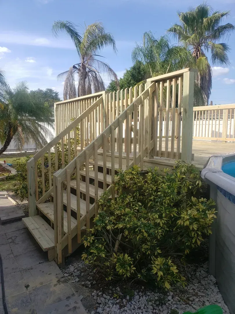 A wooden deck with stairs leading up to it and palm trees in the background.