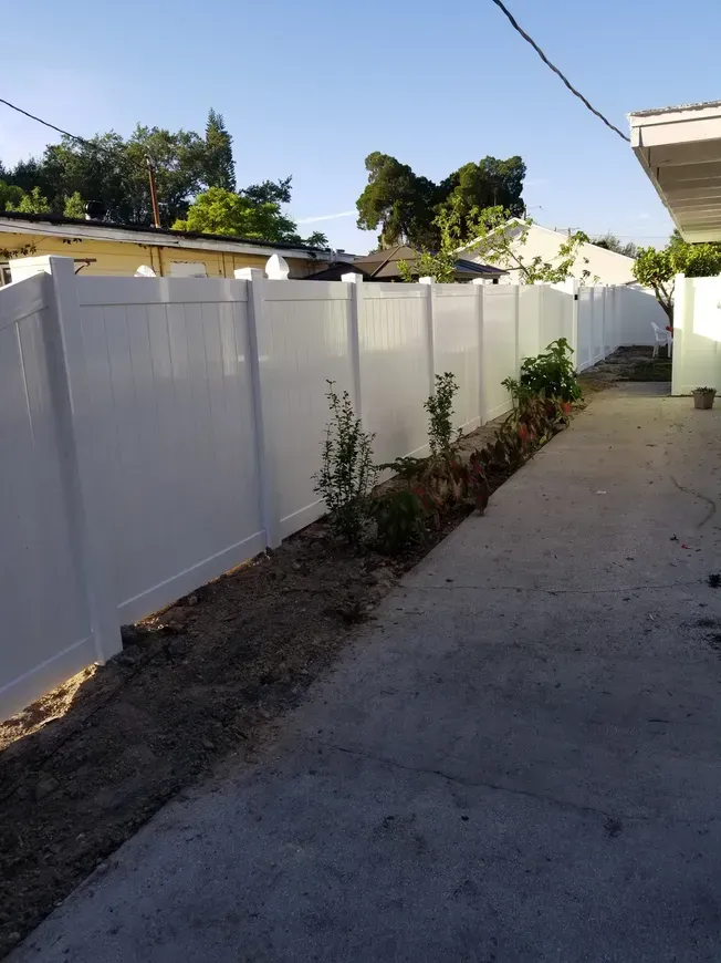 A white fence surrounds a concrete walkway leading to a house.