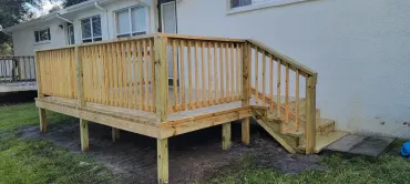 A wooden deck with stairs is in front of a white house.