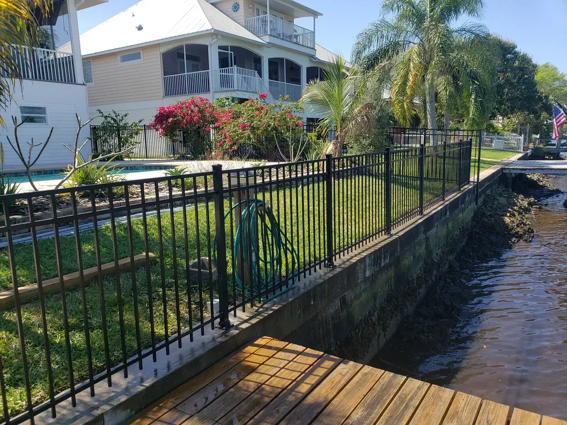 A black fence surrounds a house next to a body of water.