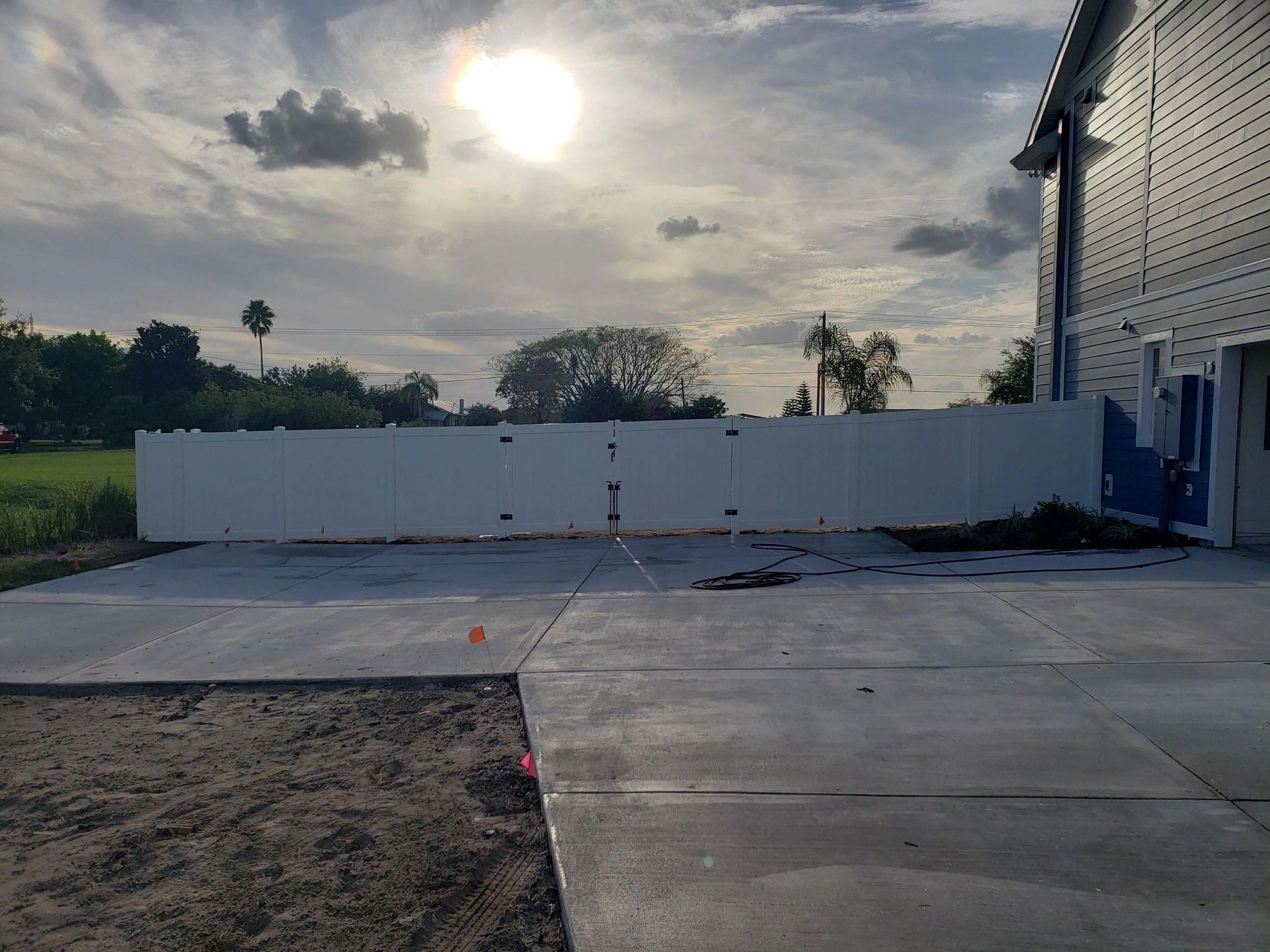 A white fence is surrounding a concrete driveway in front of a house.