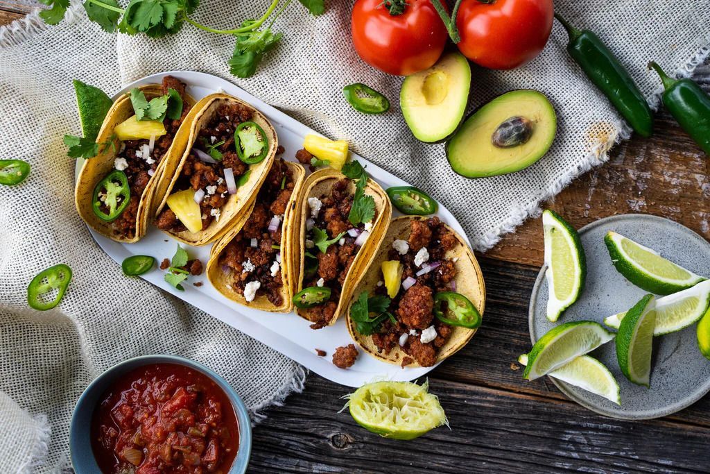 A white plate topped with tacos surrounded by vegetables and salsa.