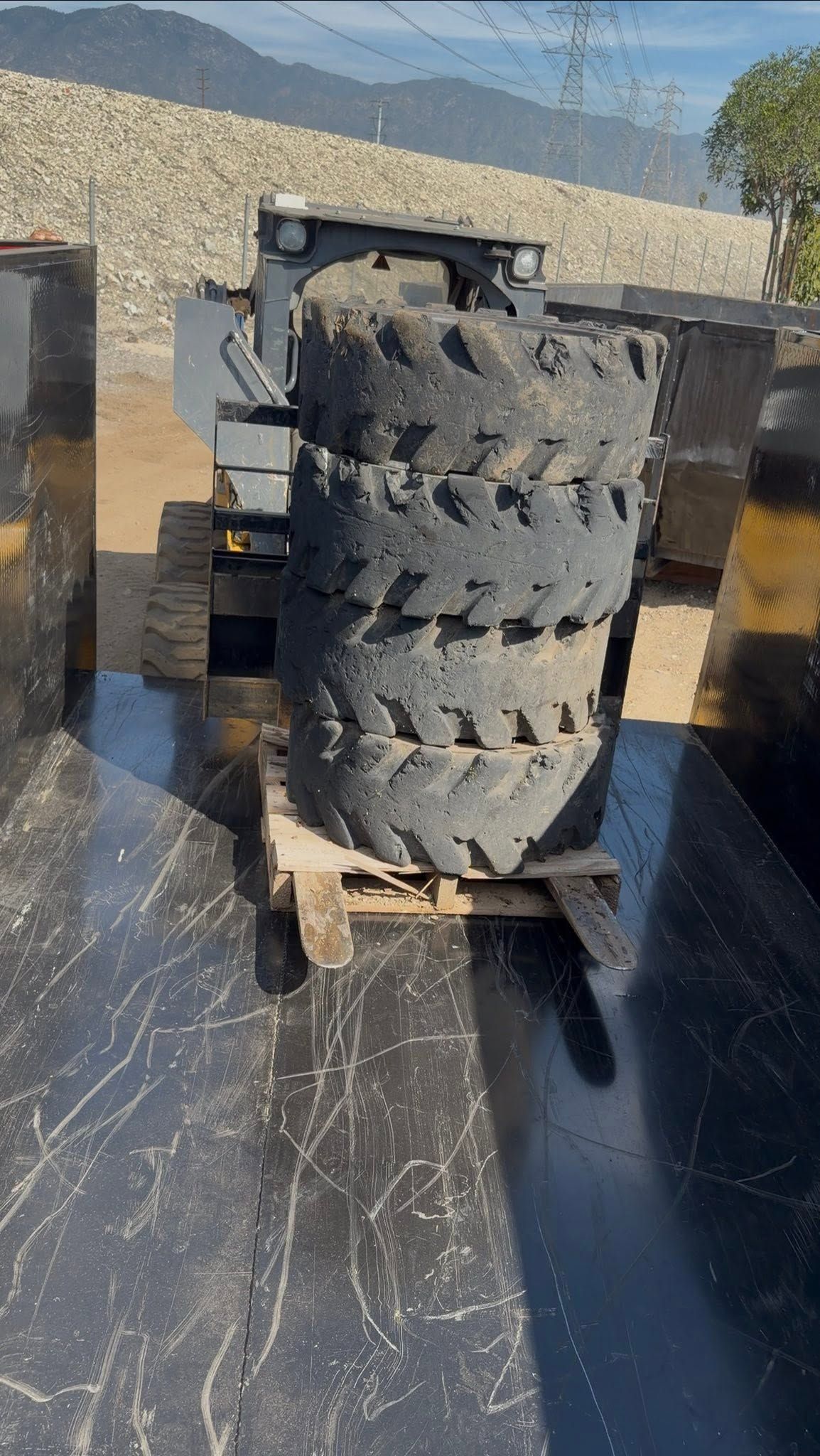 Stacked black off-road tires on a wooden pallet outdoors in bright sunlight.