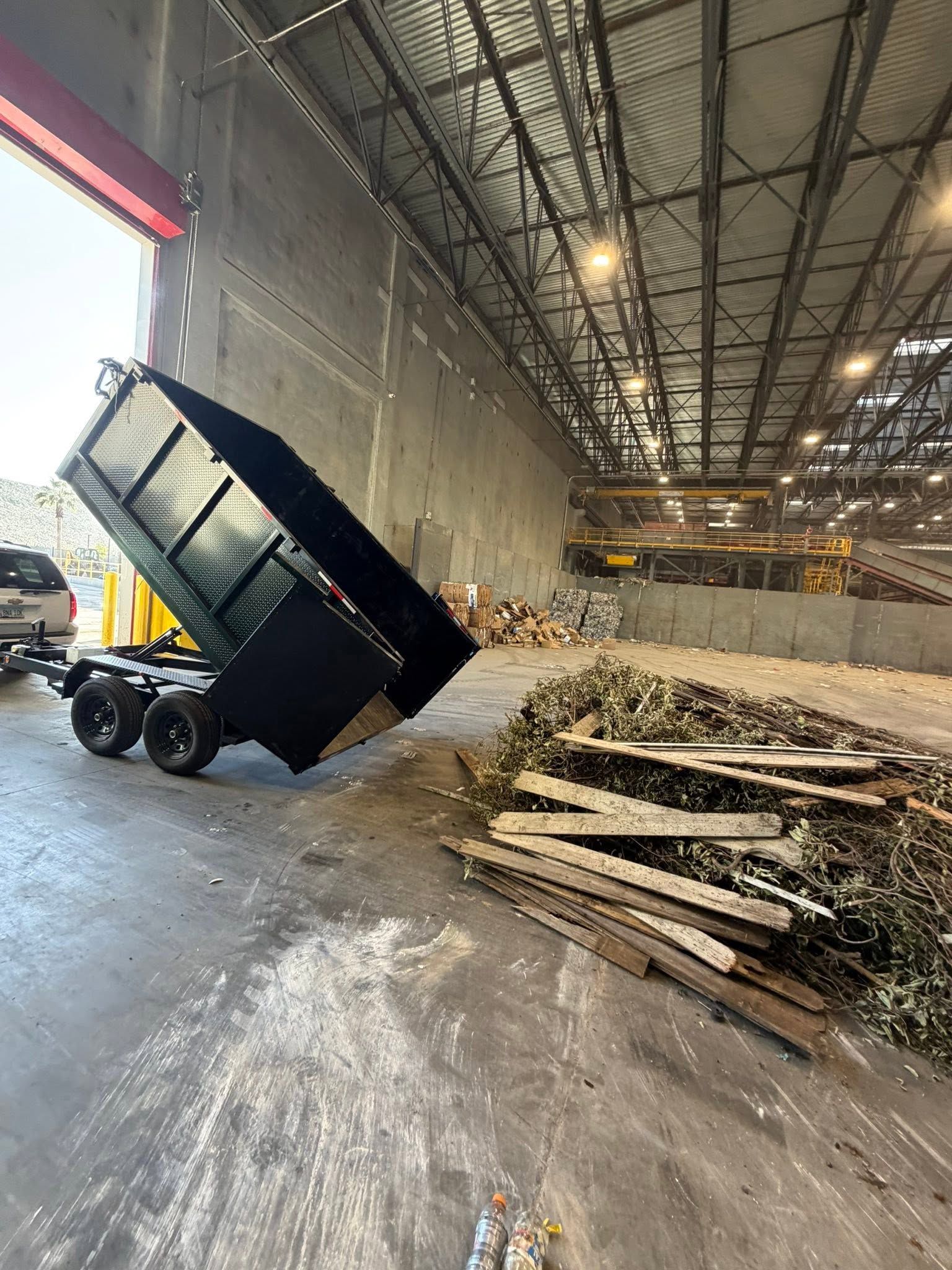 Dump truck unloading wood chips inside a warehouse, with a large pile nearby.