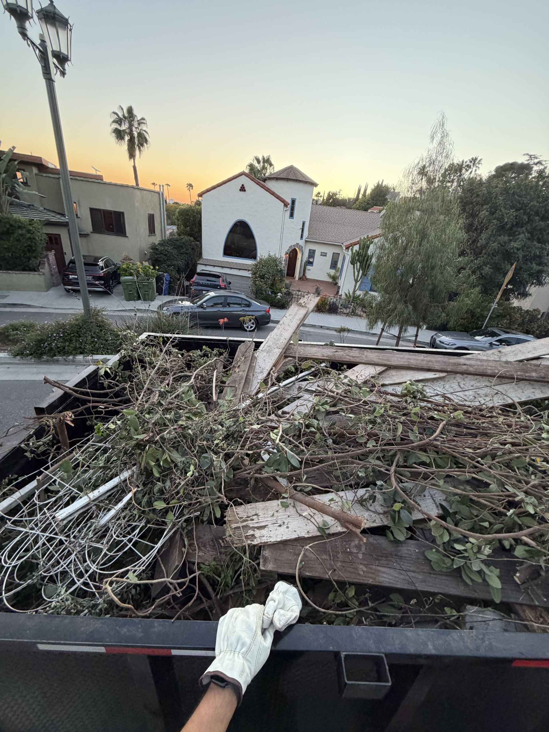 Storm debris piled in a truck bed on a suburban street at sunset.