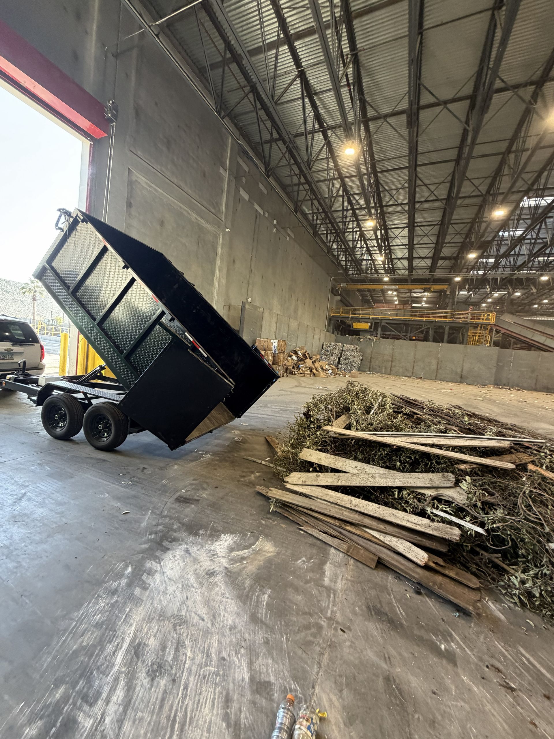 Dump truck unloading wood scraps in a large warehouse with a high ceiling.