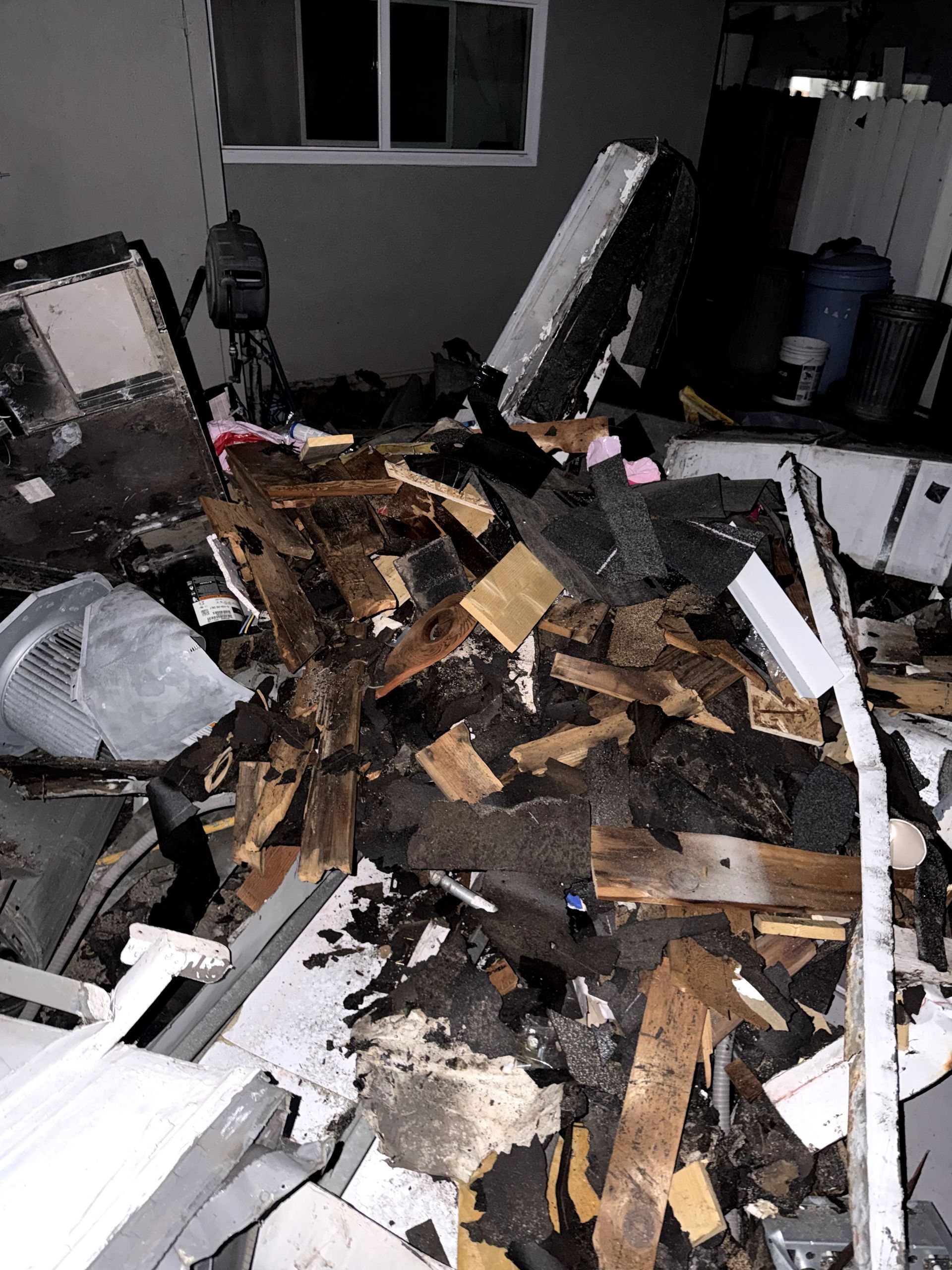 Flood-damaged room with collapsed debris, broken wood, and scattered furniture near a window.
