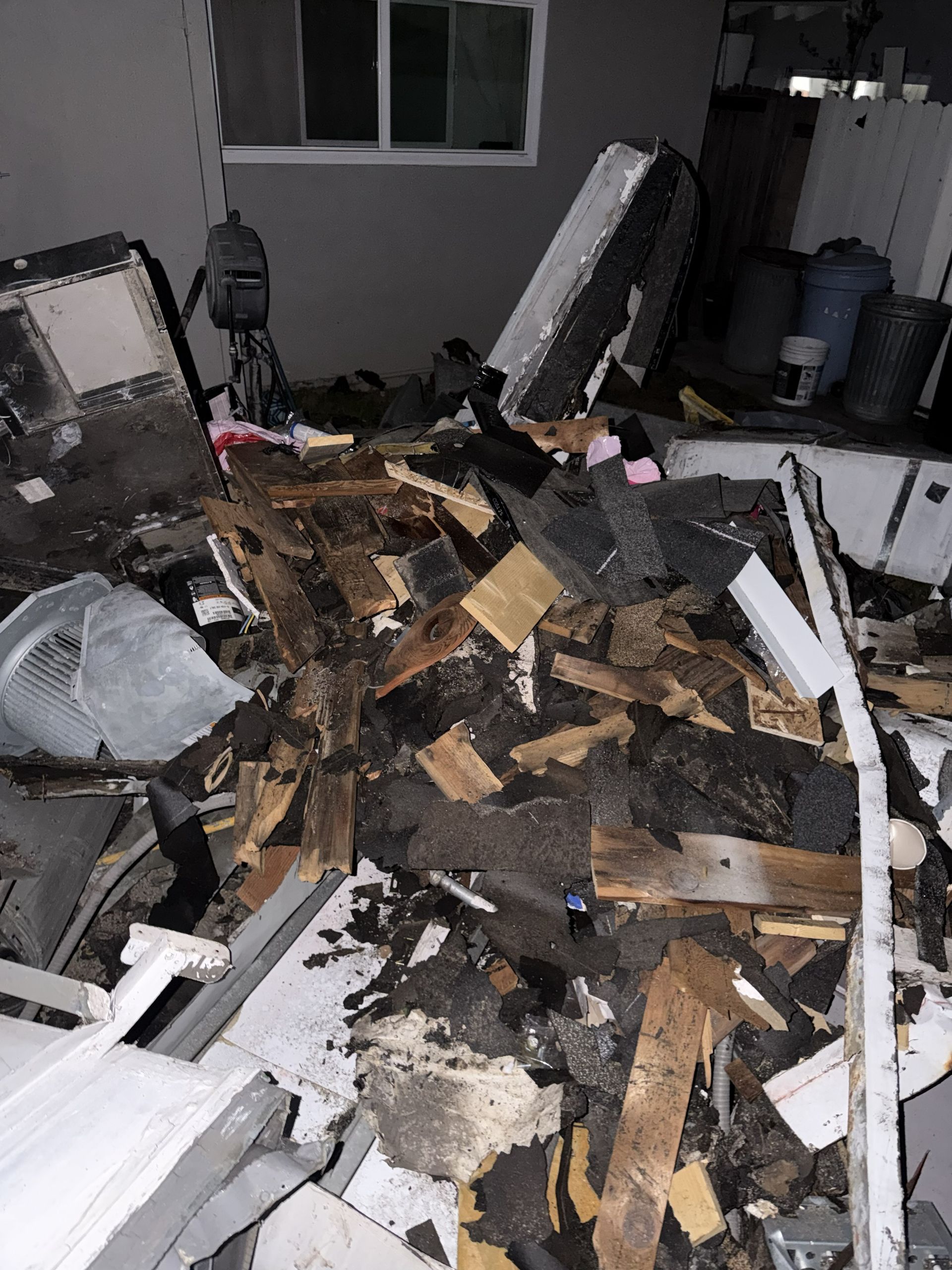 Collapsed debris and broken wood piled on a patio outside a house at night.