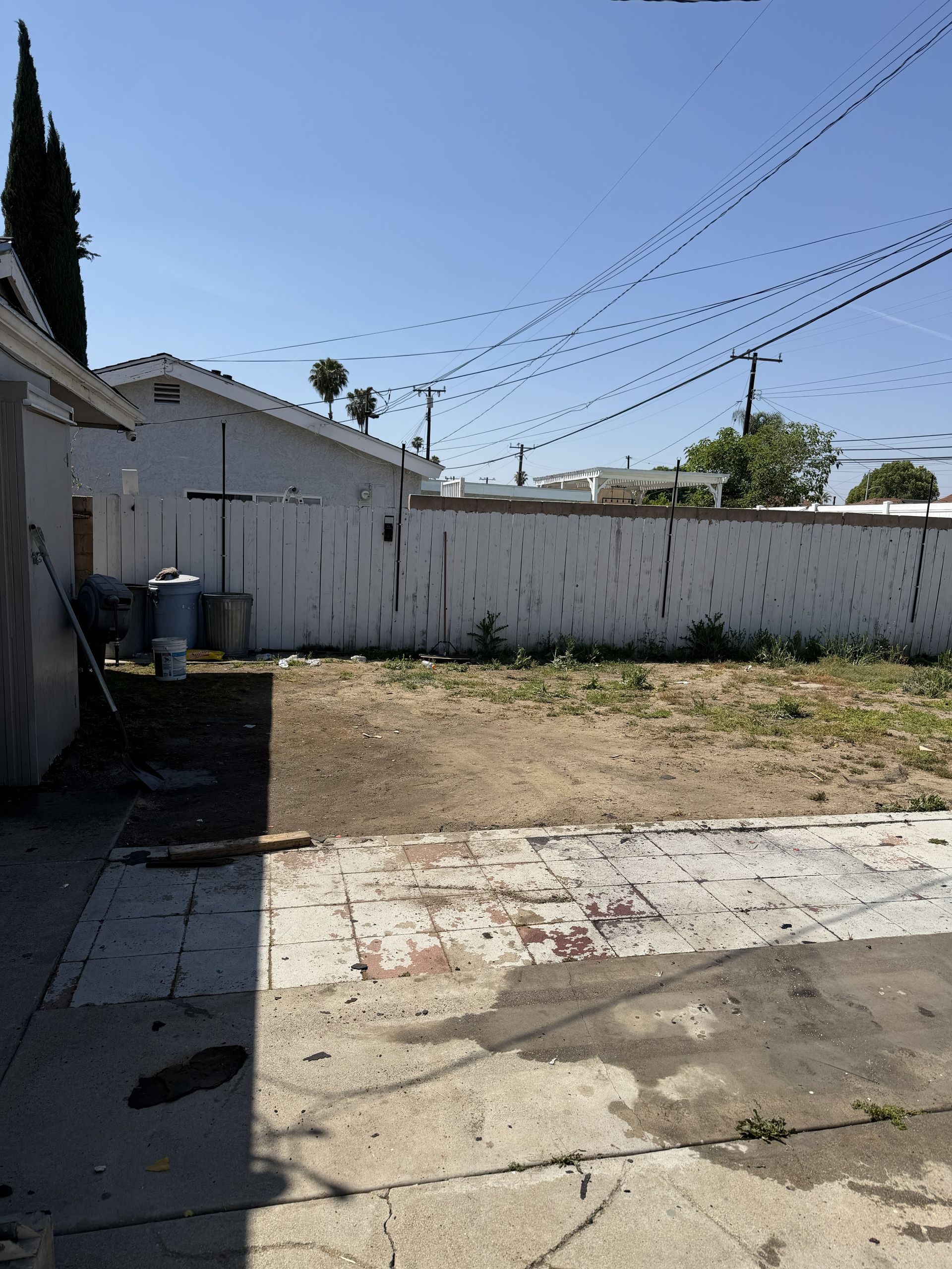 Small backyard with a concrete patio, patchy grass, white fence, and string lights overhead under a clear sky
