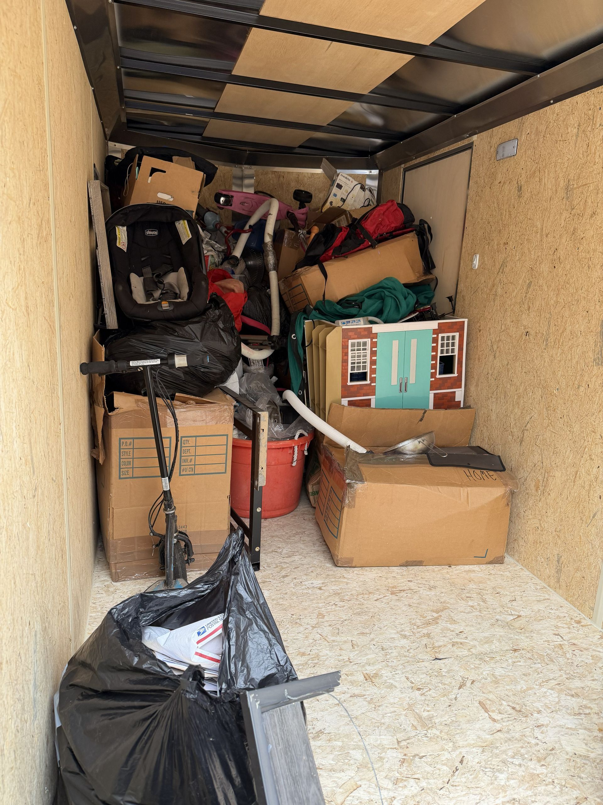 Cluttered storage trailer with stacked boxes, bags, and tools along the walls.