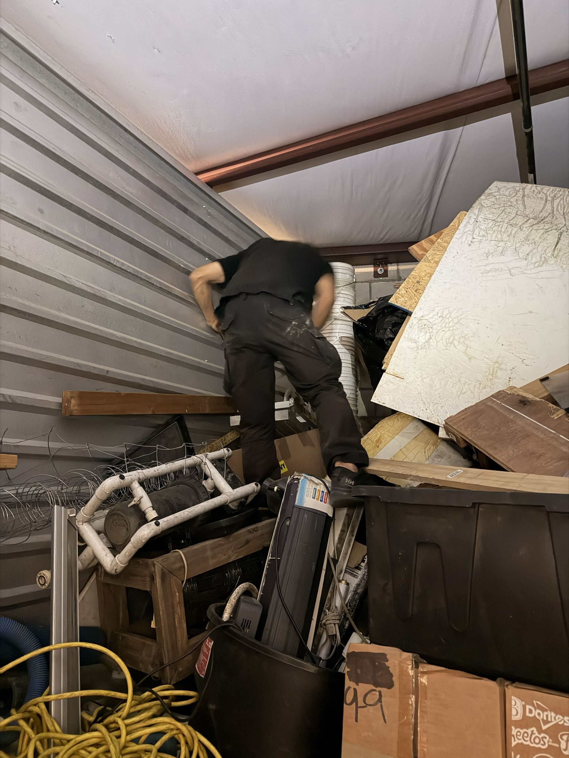 Worker climbing through debris in a damaged attic with a collapsed ceiling.
