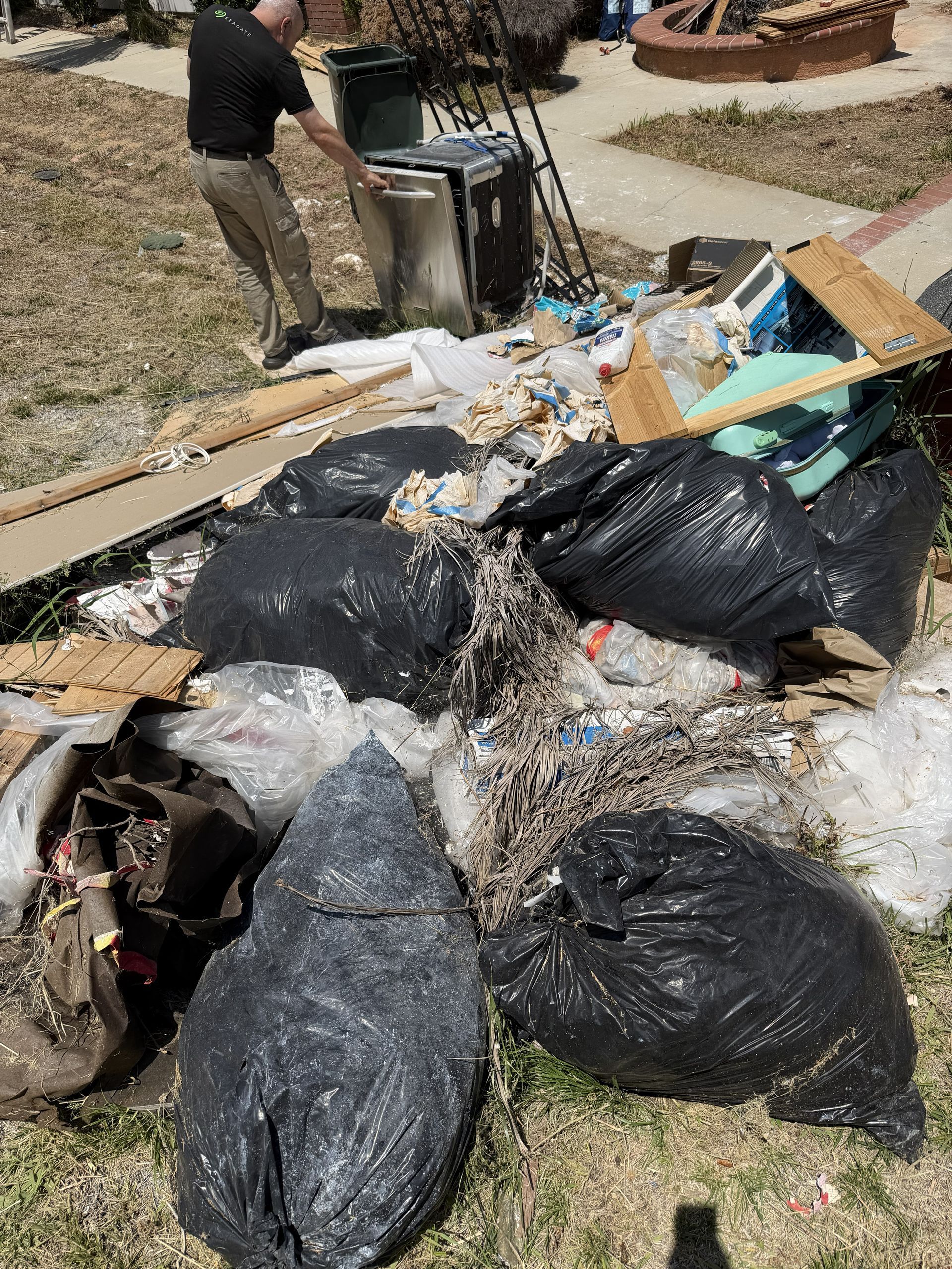 Trash bags and scattered debris piled beside a sidewalk, with a person standing nearby.