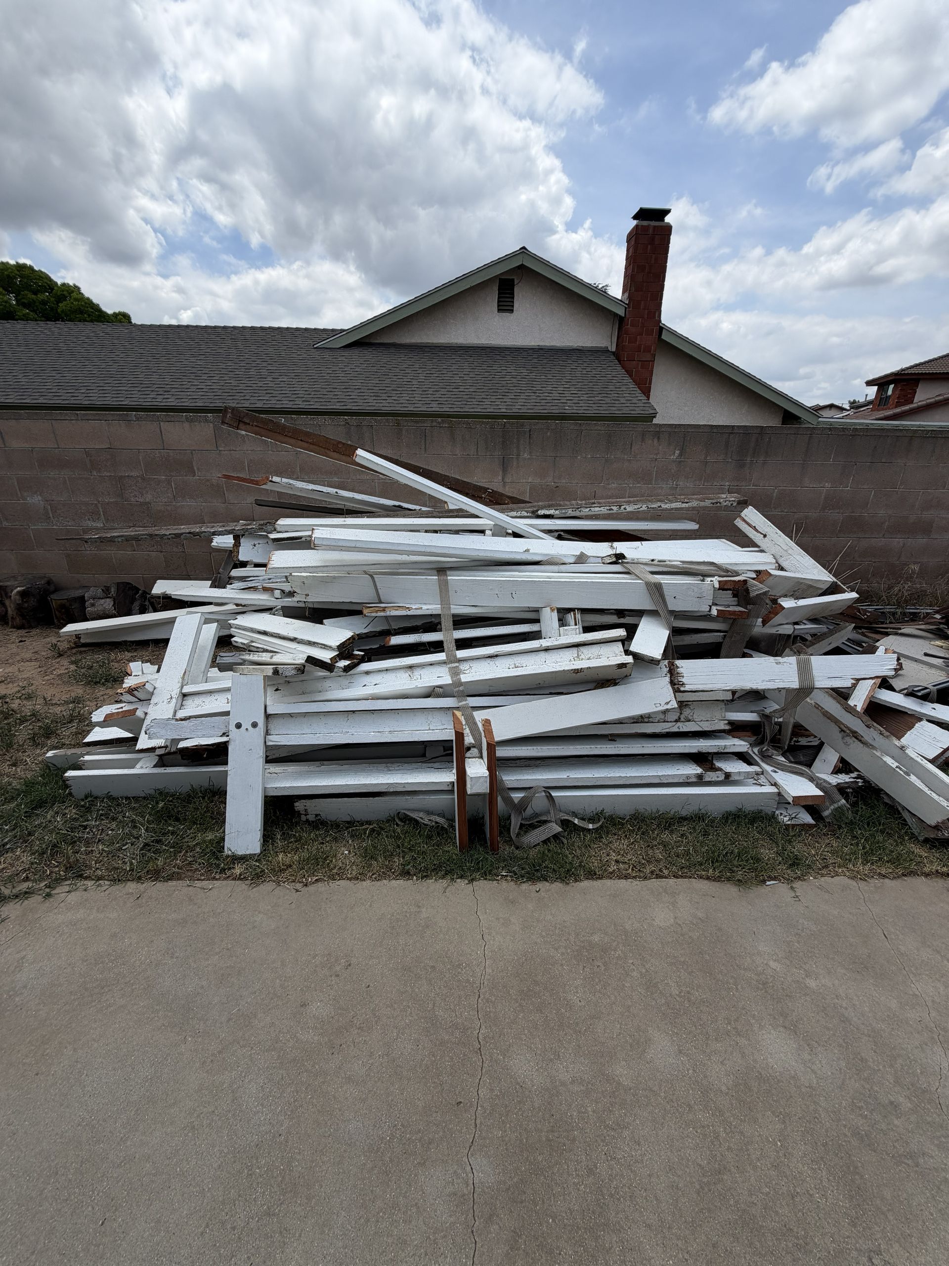Stacked white wooden boards beside a house with a brick chimney and gravel driveway