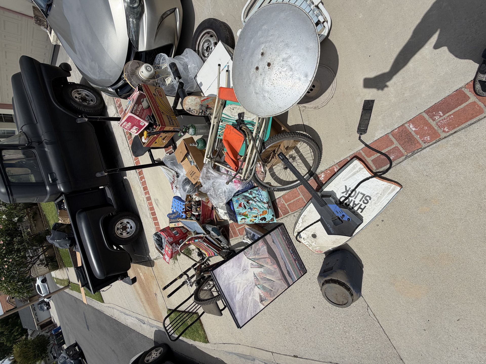 Scattered outdoor yard sale items on a sidewalk, including lamps, chairs, and assorted household goods.