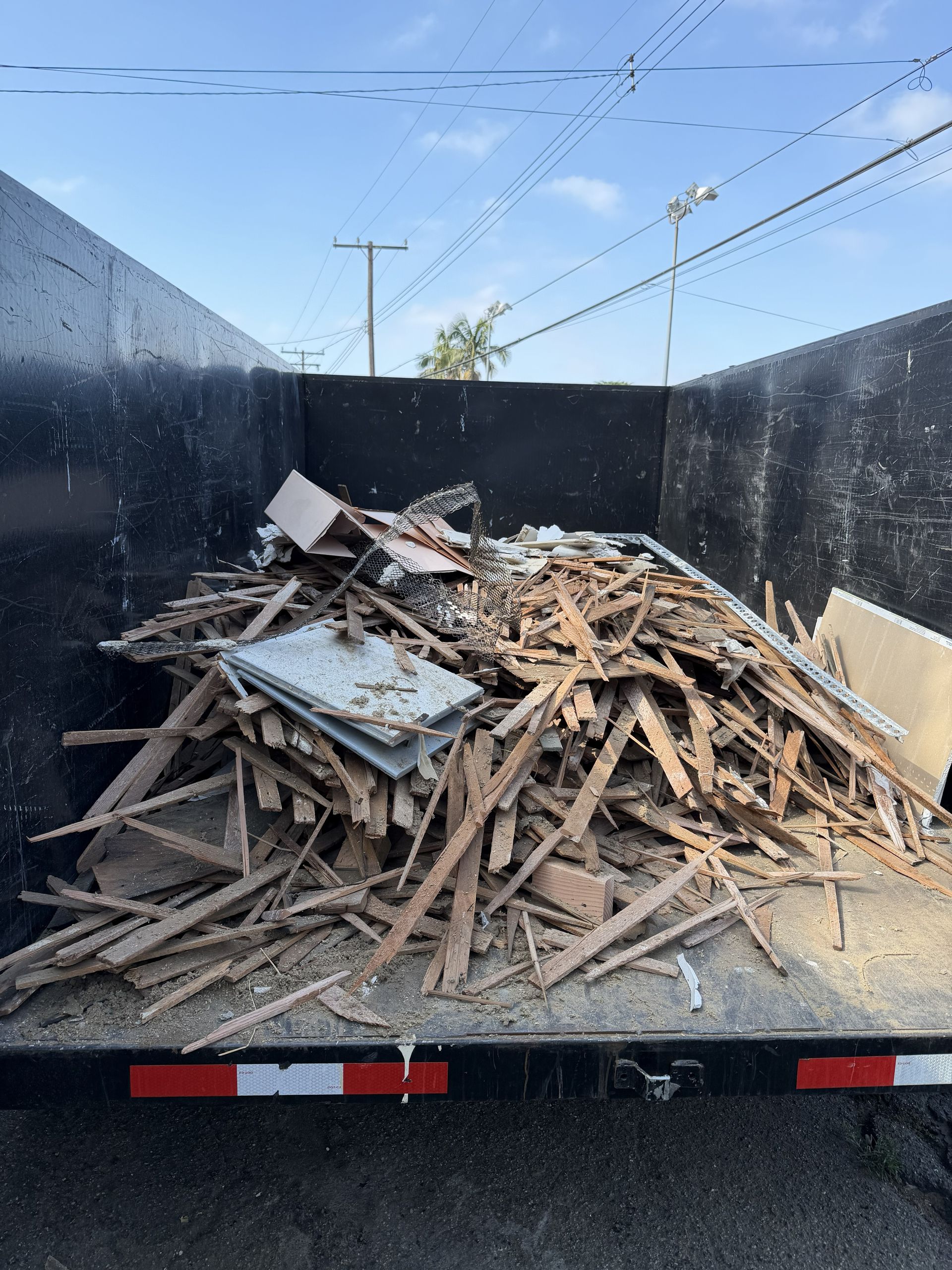 Truck bed filled with broken wood debris and scrap metal against a black liner, viewed from behind