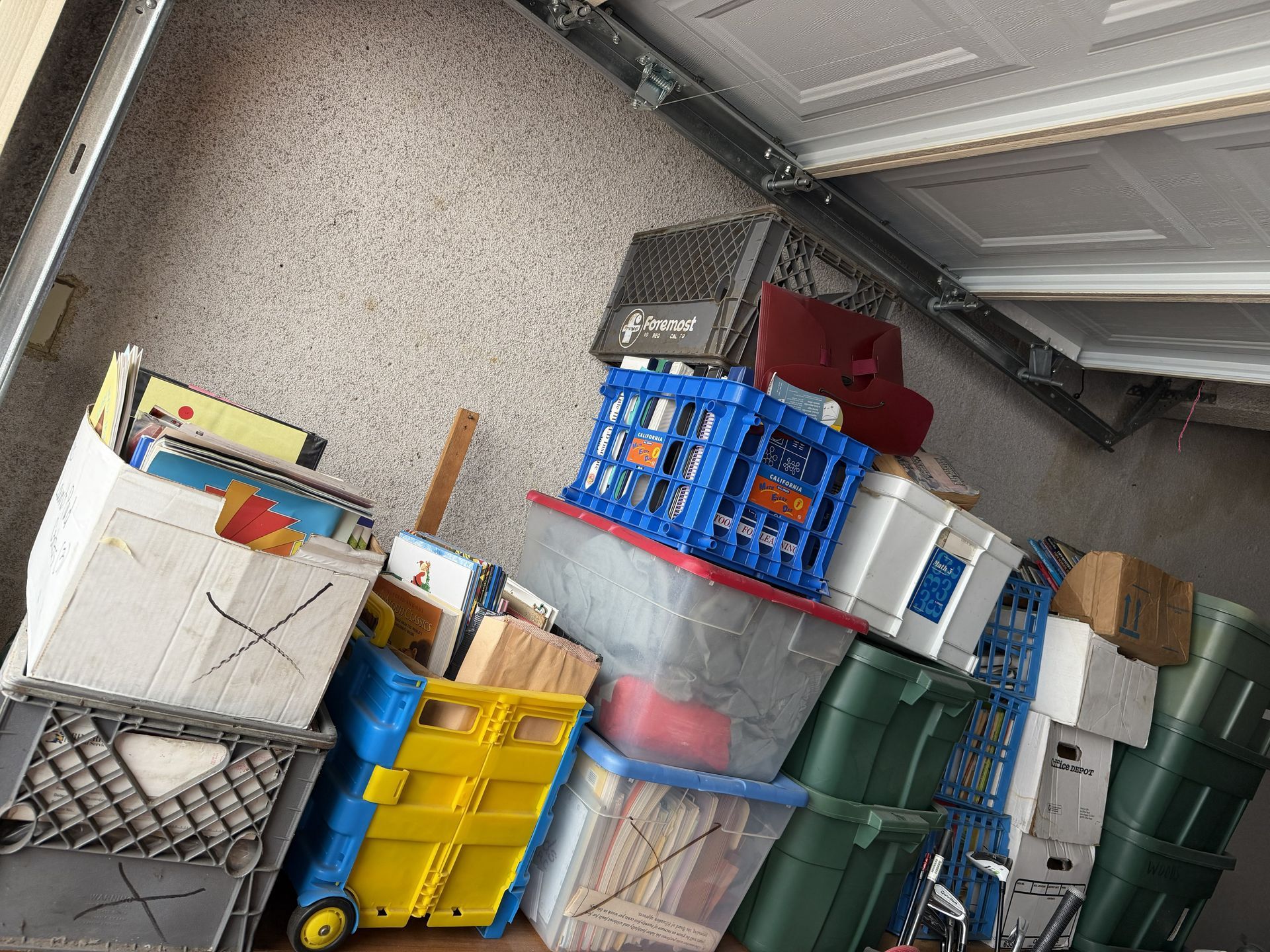 Cluttered garage with stacked plastic bins, boxes, and storage crates under a garage door