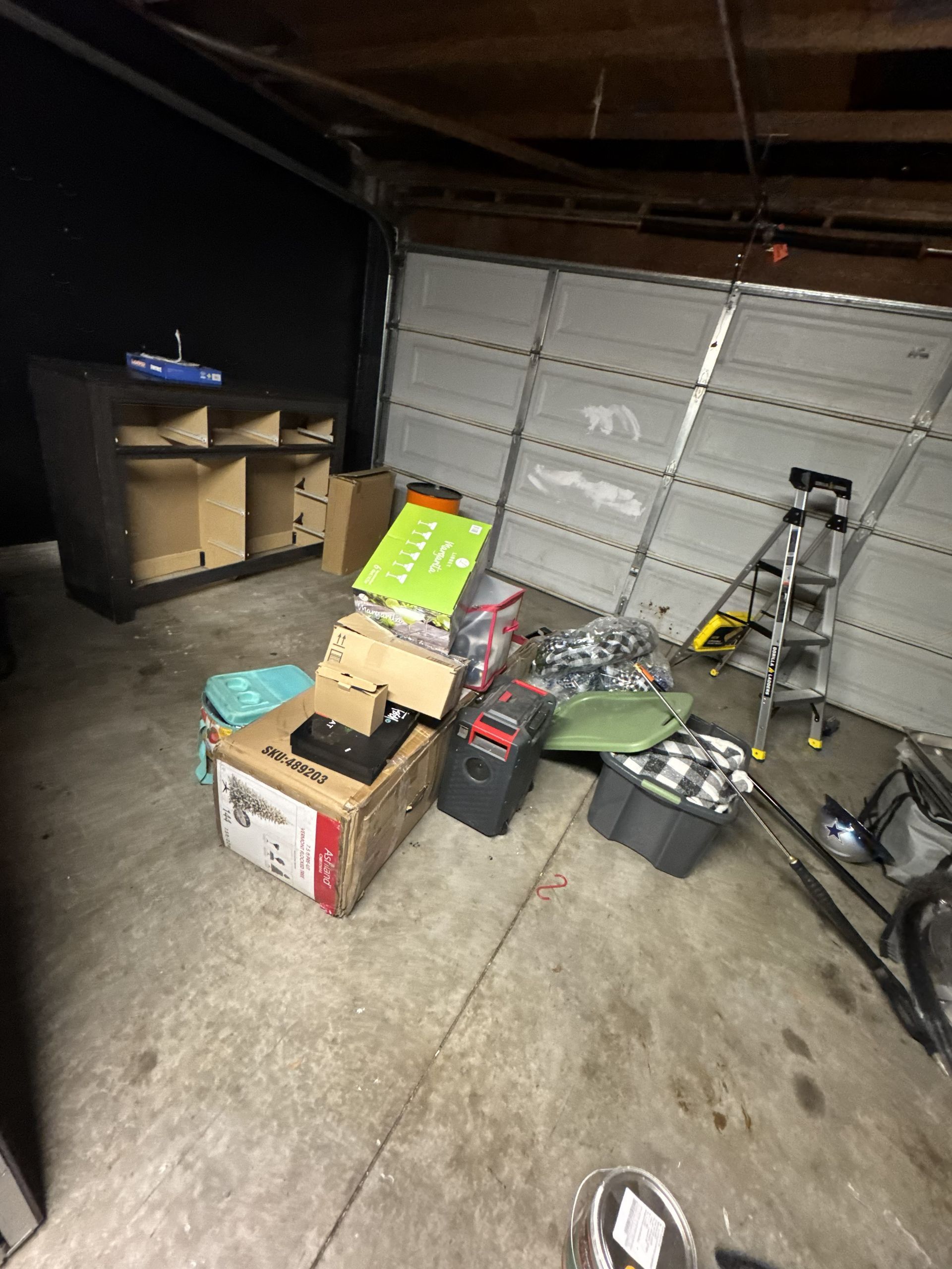 Cluttered garage with boxes, tools, a ladder, and a bicycle near a closed garage door.