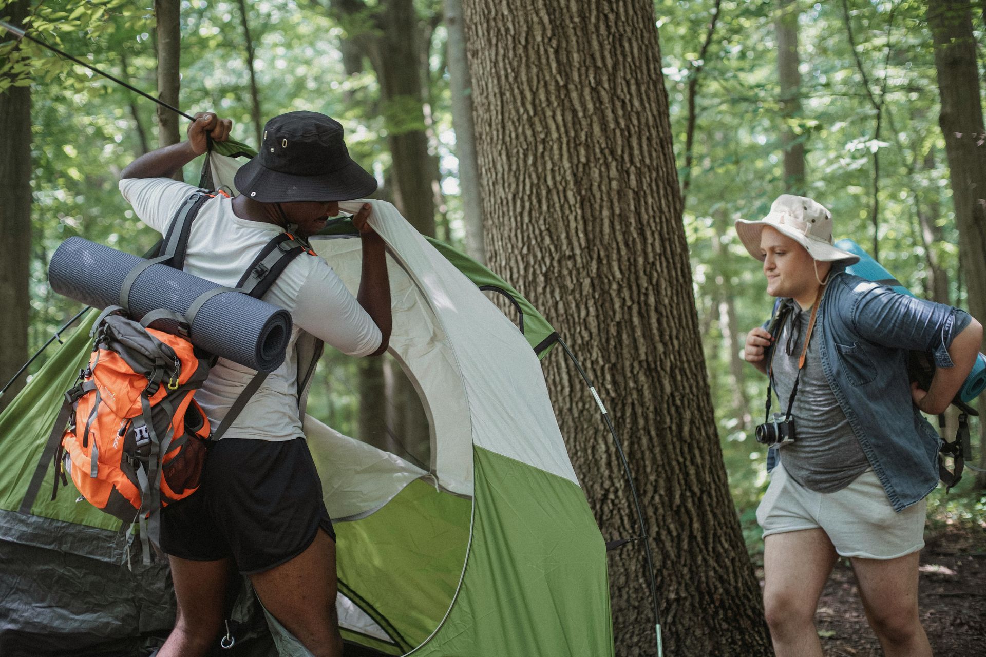 A man and a woman are setting up a tent in the woods.
