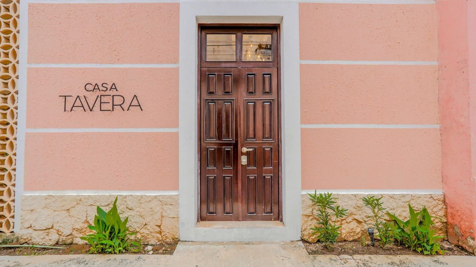 Fachada rosa con una puerta central de madera y las palabras «Casa Tavera» a la izquierda.