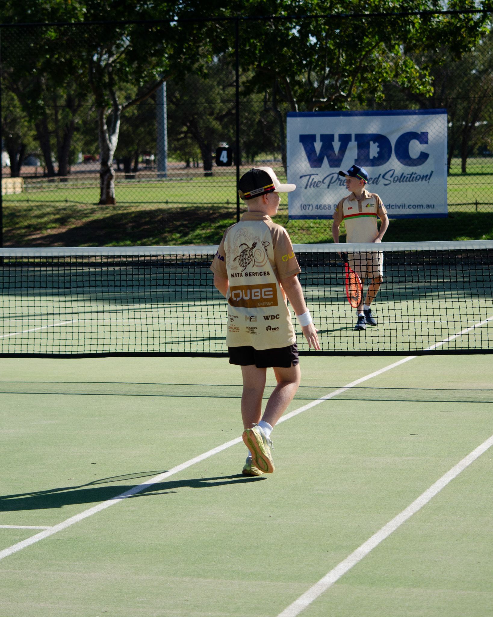 Two people on a tennis court with a net and a WDC banner in the background.