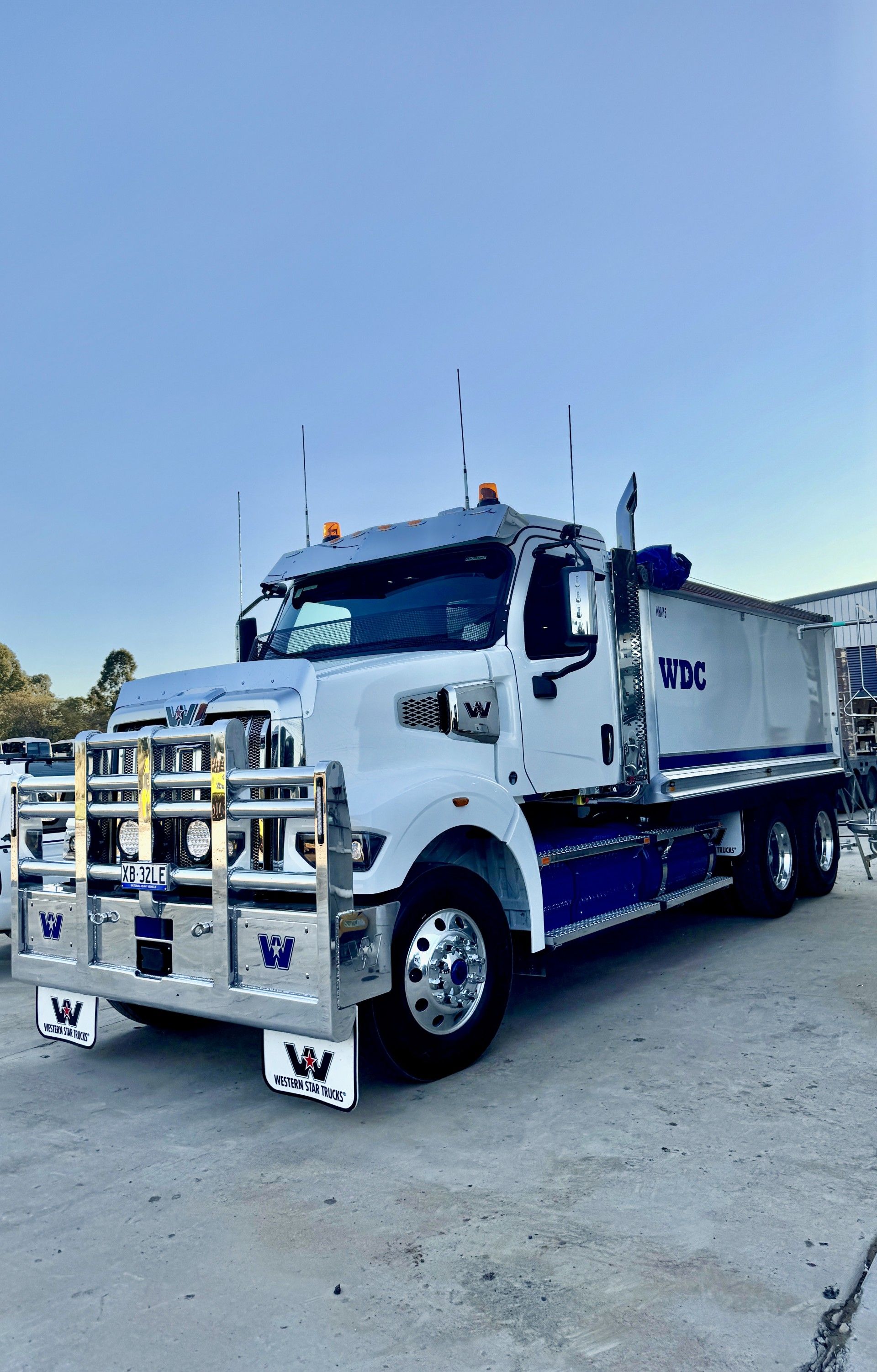 White cargo truck with chrome bull bar parked on a gravel lot under a clear blue sky