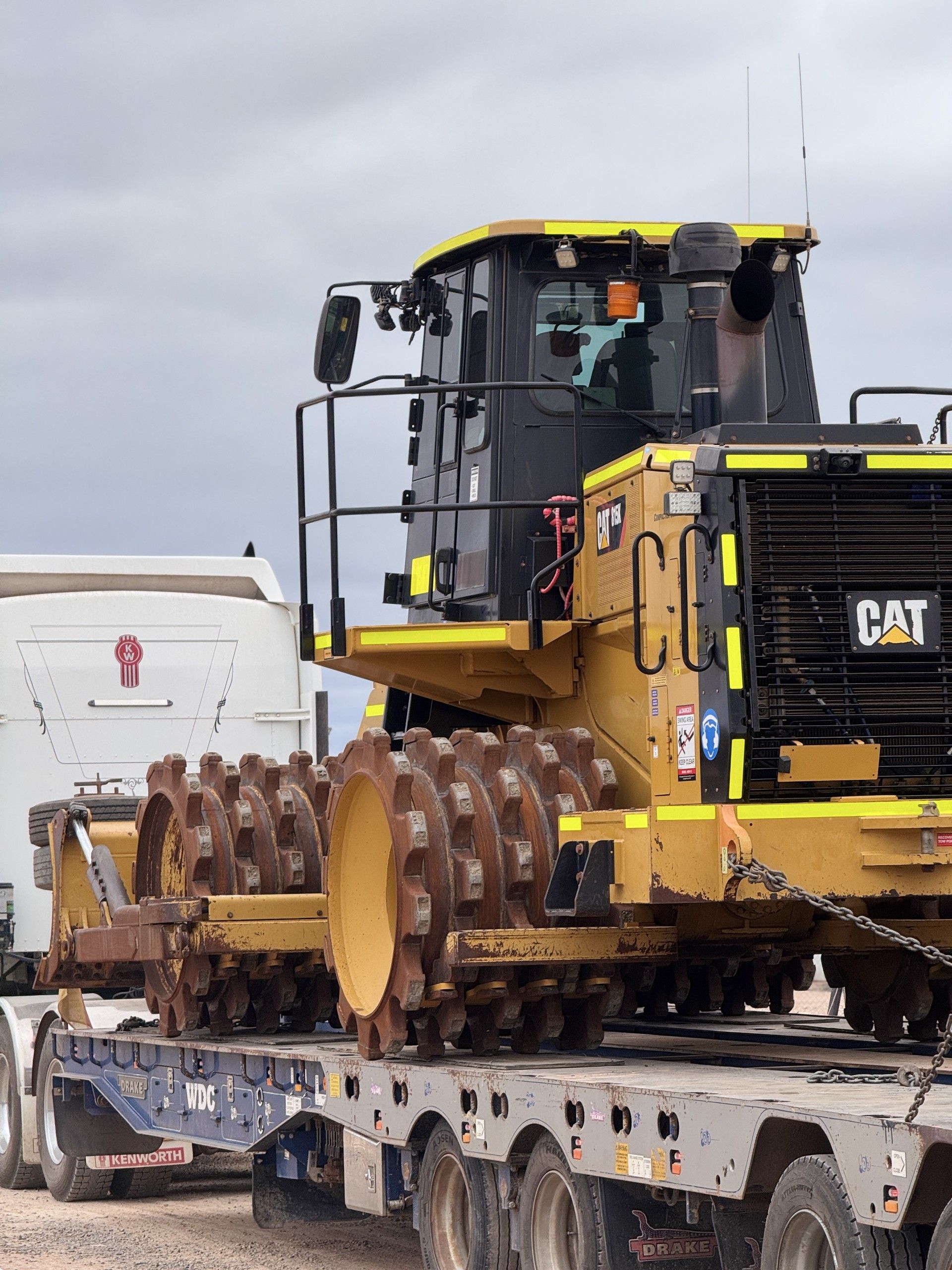 Yellow CAT bulldozer secured on a flatbed trailer in a cloudy outdoor setting