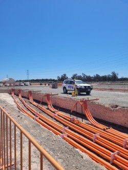 Orange utility conduits lined in a trench at a construction site, with a pickup truck in the background.