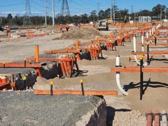 Orange utility markers and trenches on a gravel construction site with equipment in the distance