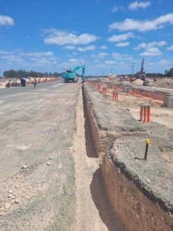 Construction site with trench excavation, gravel roadway, and a blue excavator under a clear sky
