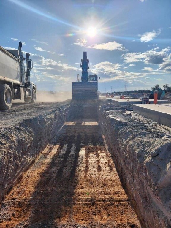 Bulldozer leveling dirt trench at a construction site under bright sun, with a truck nearby