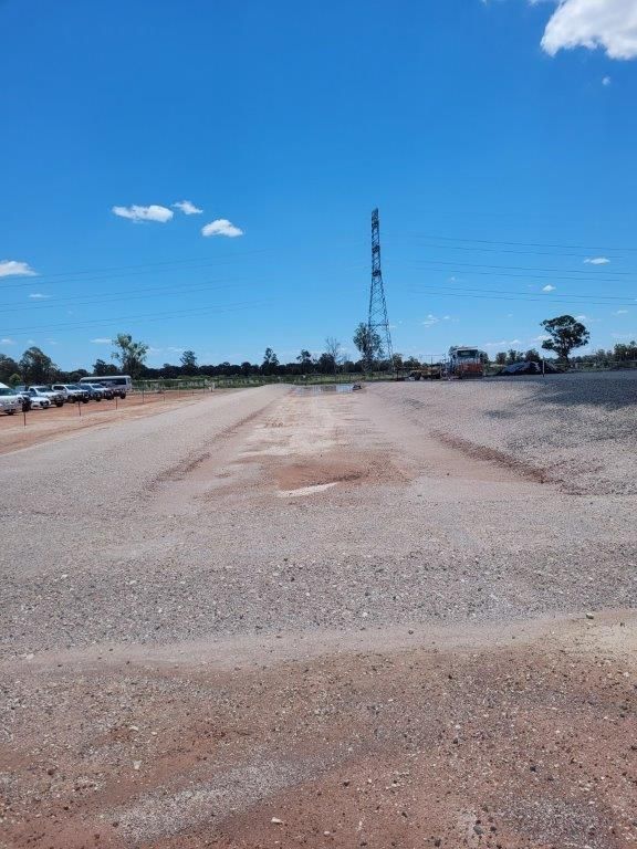 Wide gravel lot under a bright blue sky, with a tall utility tower in the distance.
