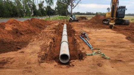 Long concrete pipe laid in a dirt trench at a construction site with excavators and tools nearby
