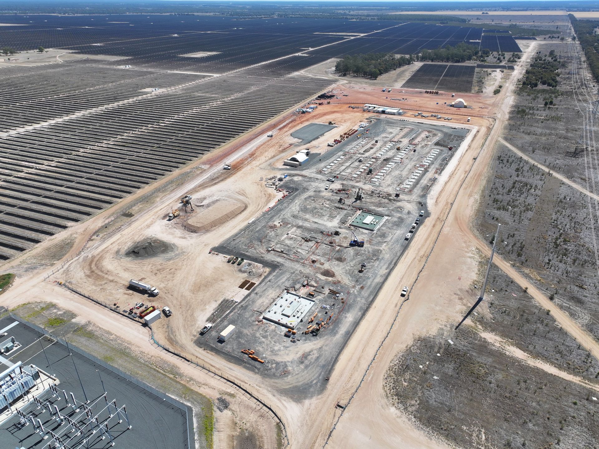 Aerial view of a large construction site beside a solar farm and road, with excavation and equipment visible