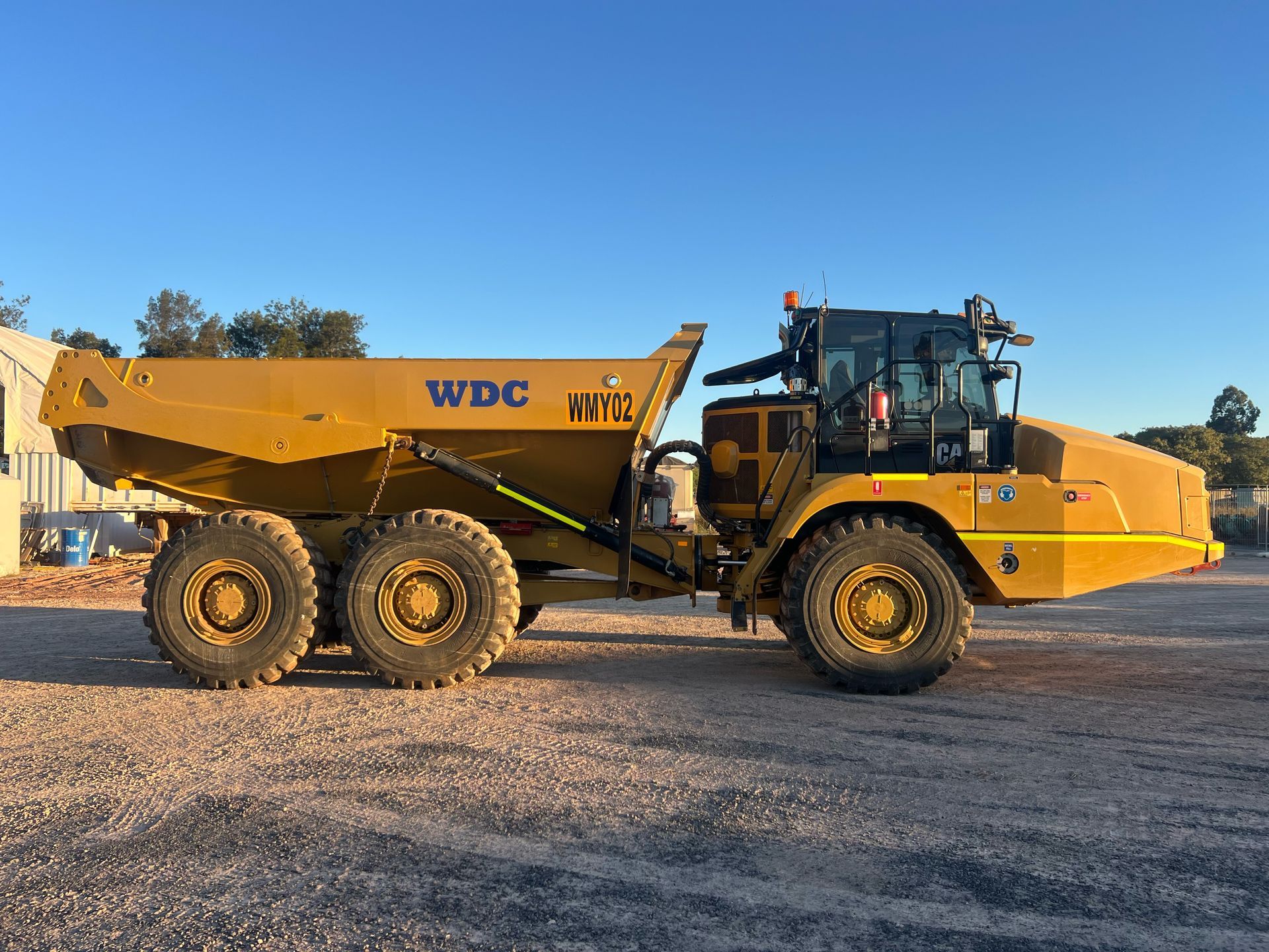 Yellow WDC dump truck parked on a gravel lot under a clear blue sky