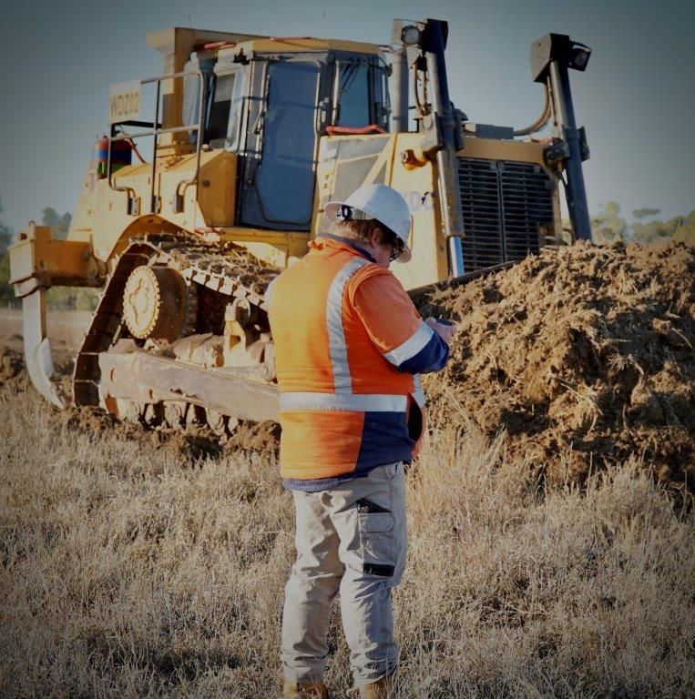 Construction worker in orange vest inspecting a bulldozer at a dirt worksite