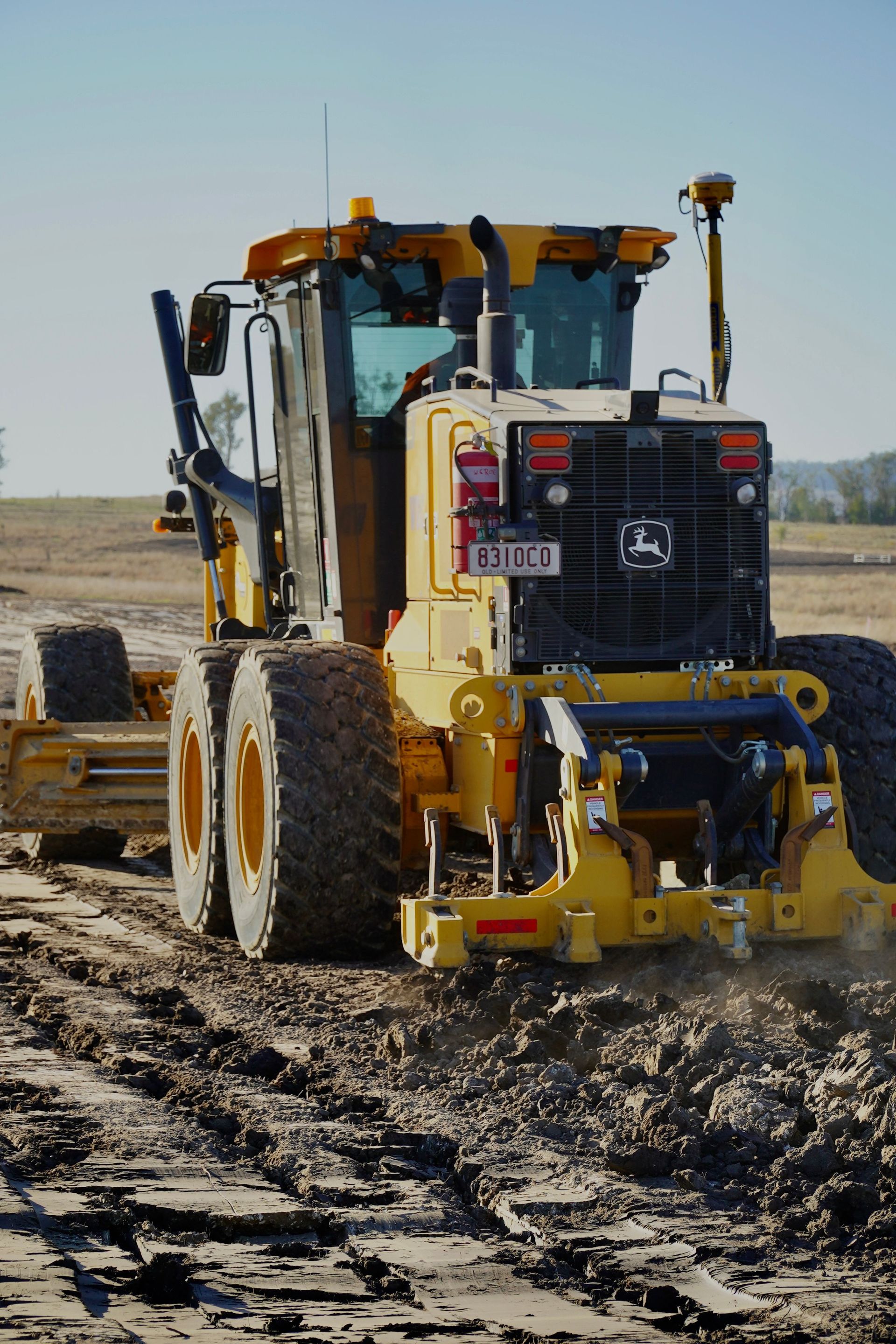Yellow road grader leveling muddy dirt on a construction site