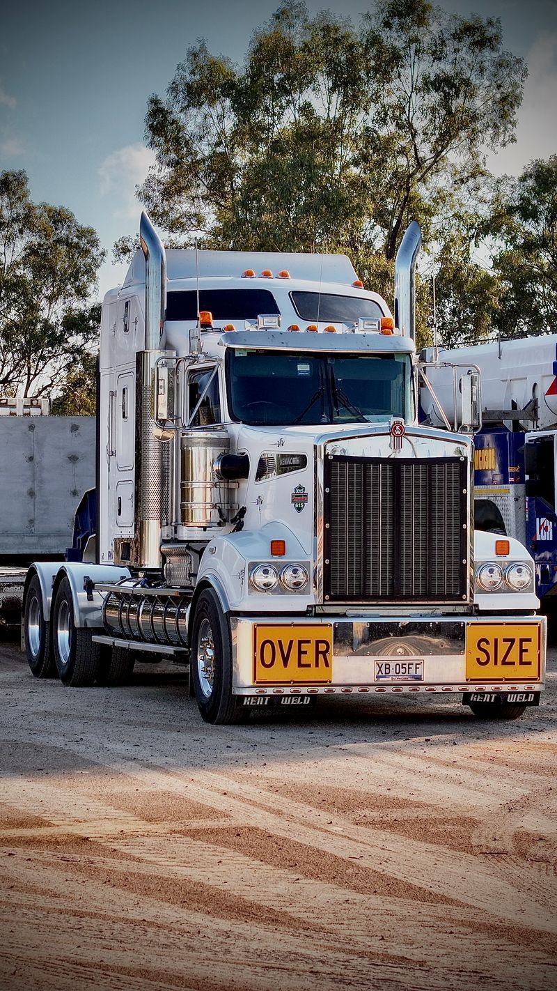White semi-truck hauling an oversized load, with yellow “OVER SIZE” signs on front bumper.