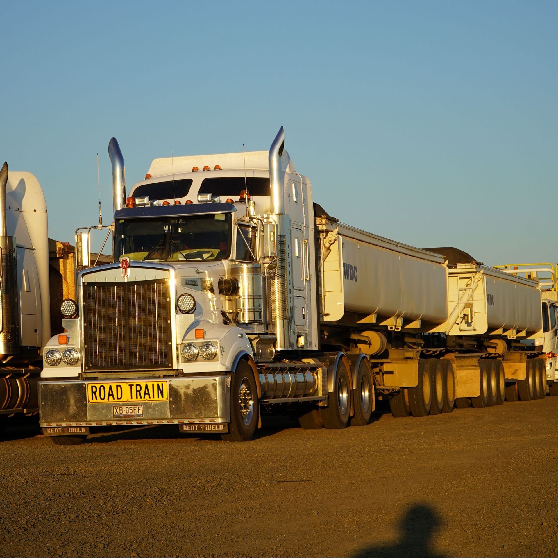 White road train semi truck driving on a dirt road at sunset